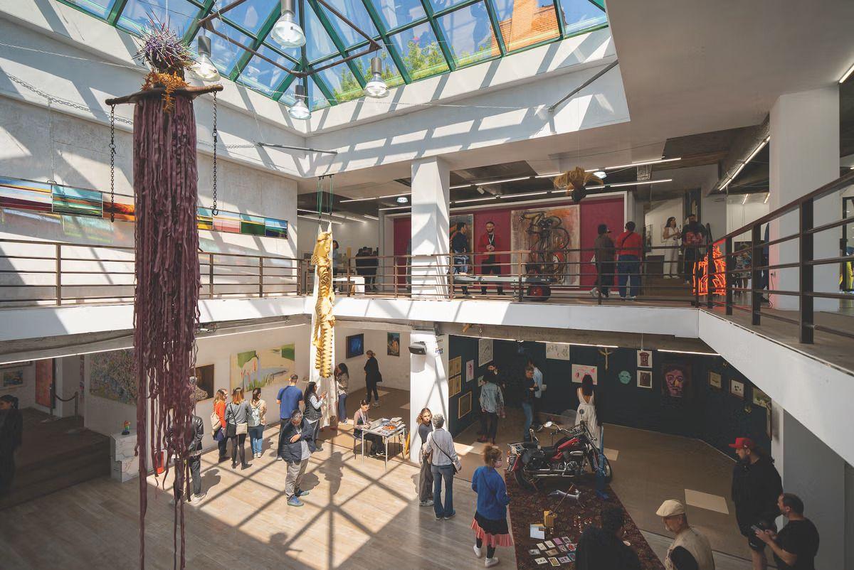 Bright, spacious art gallery with visitors viewing diverse contemporary works under a glass skylight.